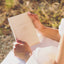 bride holding wedding vow book that says my promises to him, her wedding vows, book is cream and writing is gold
